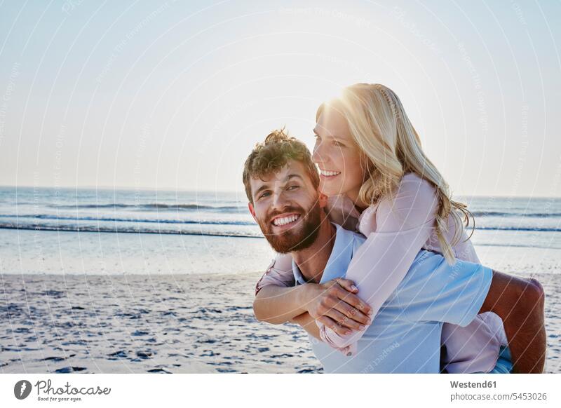 Porträt eines glücklichen Paares am Strand lächeln Glück glücklich sein glücklichsein Pärchen Partnerschaft Beach Straende Strände Beaches Huckepack Mensch