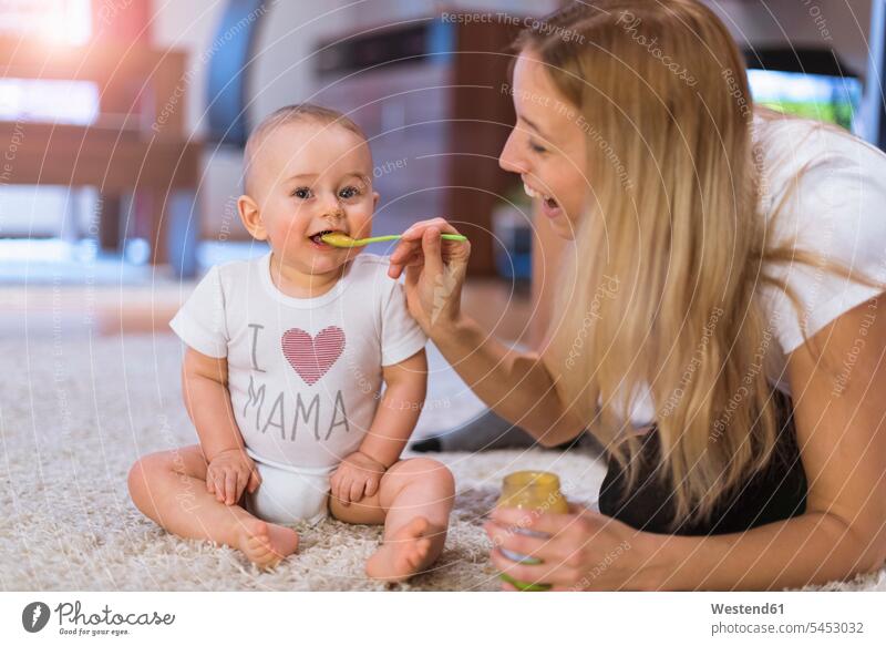 Mutter füttert ihren kleinen Sohn zu Hause Teppich Teppiche Söhne Mami Mutti Mütter Mama Baby Babies Babys Säuglinge Kind Kinder füttern essen essend Boden