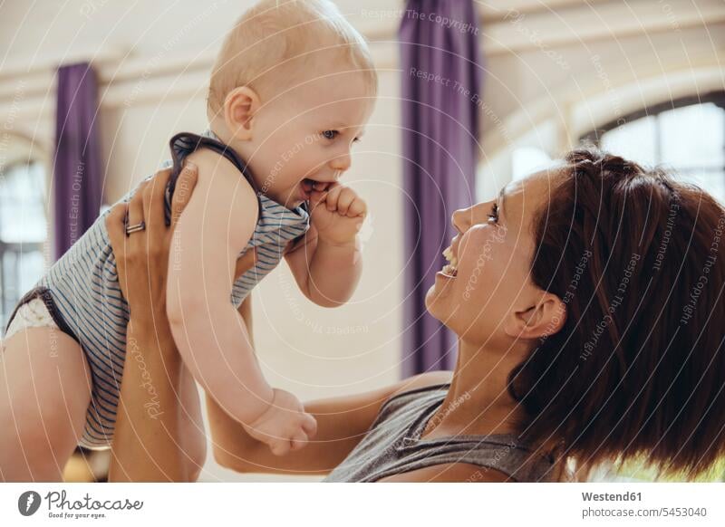 Sportliche Frau hebt glückliches Baby im Trainingsraum hoch trainieren lachen heben Babies Babys Säuglinge Kind Kinder Mutter Mami Mutti Mütter Mama Spaß Spass