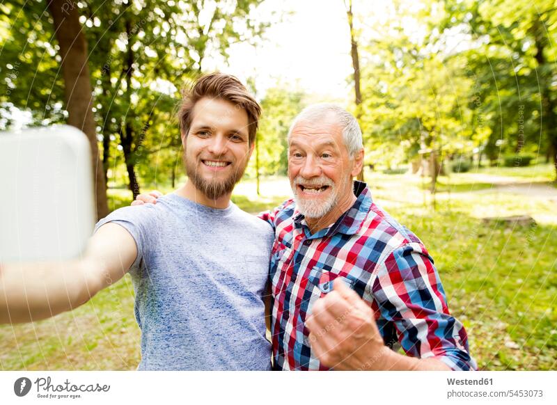 Porträt eines älteren Vaters und seines erwachsenen Sohnes, die ein Selfie in einem Park machen Selfies Papas Väter Vati Vatis Papis Eltern Familie Familien