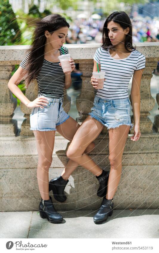 Zwei Zwillingsschwestern im Freien bei einem Getränk zum Mitnehmen Getraenk Getränke Getraenke Schwester Schwestern Freundinnen trinken Food and Drink
