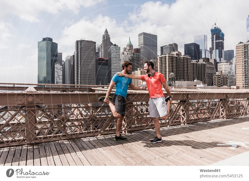 USA, New York City, zwei Athleten strecken sich auf der Brooklyn Brige Brücke Bruecken Brücken Mann Männer männlich Freunde Joggen Jogging Kopfhörer Kopfhoerer