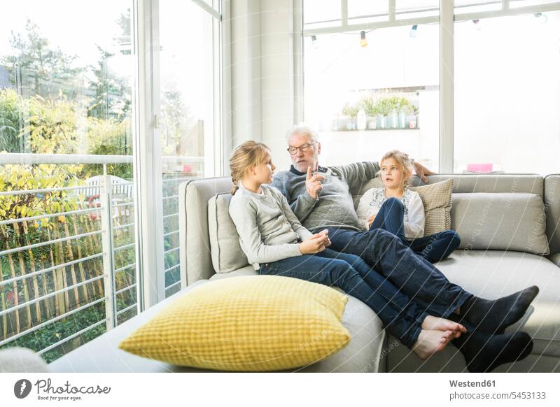 Großvater im Gespräch mit zwei Mädchen auf dem Sofa im Wohnzimmer Wohnraum Wohnung Wohnen Wohnräume Wohnungen weiblich Couches Liege Sofas Opa Großpapa