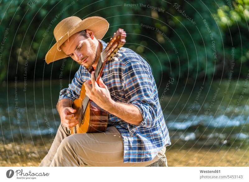 Mann spielt Gitarre am Flussufer Männer männlicher Erwachsener männliche Erwachsene musizieren Musik machen Gitarren Gitarrist Gitarrenspieler Gitarristen