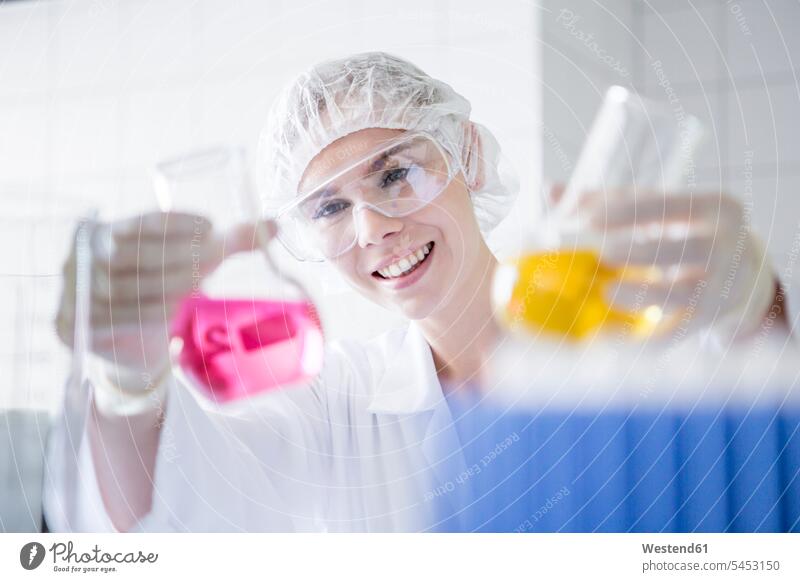 Lächelnder Wissenschaftler im Labor hält zwei Becher mit Flüssigkeiten hoch lächeln arbeiten Arbeit wissenschaftlich Wissenschaften halten flüssig Becherglas