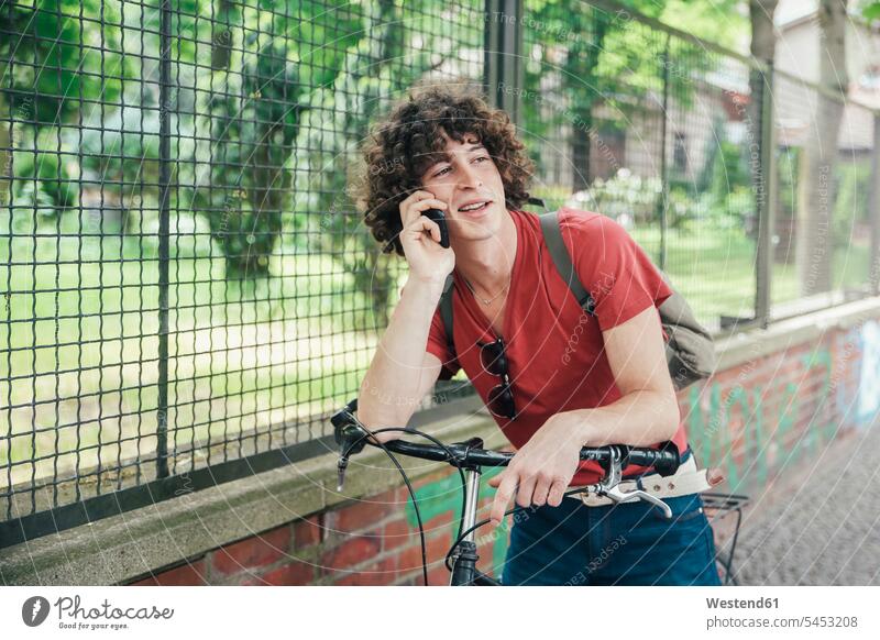 Junger Mann mit Fahrrad am Telefon Handy Mobiltelefon Handies Handys Mobiltelefone telefonieren anrufen Anruf telephonieren Männer männlich Bikes Fahrräder