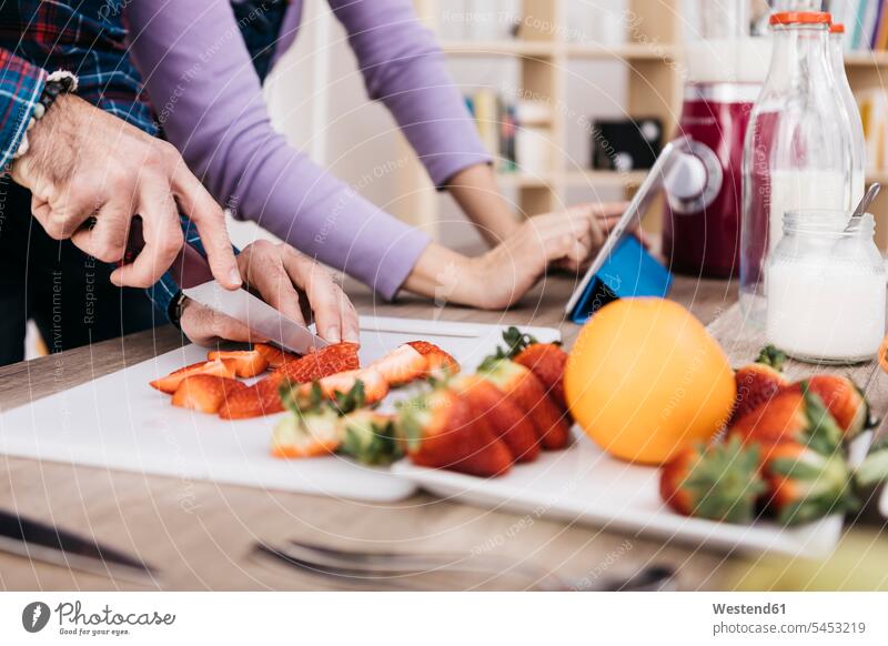 Mann hackt Erdbeeren, während seine Freundin eine Tablette benutzt, Teilansicht zubereiten kochen Essen zubereiten Hand Hände Zubereitung Mensch Menschen Leute