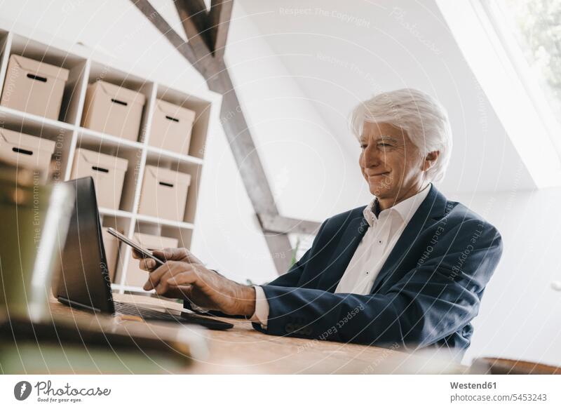 Lächelnder Senior-Geschäftsmann benutzt Laptop in seinem Büro Office Büros Businessmann Businessmänner Geschäftsmänner Arbeitsplatz Arbeitsstätte Arbeitstelle