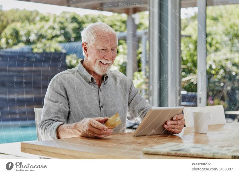 Älterer Mann sitzt auf der Terrasse und macht Online-Zahlungen mit Kreditkarte bezahlen Senior ältere Männer älterer Mann Senioren sitzen sitzend Terrassen
