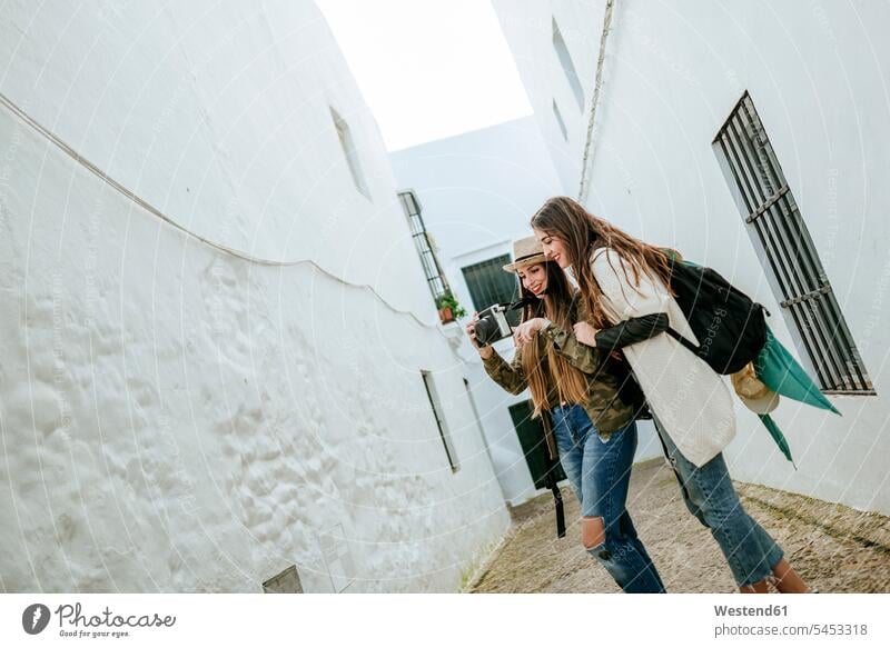 Zwei glückliche junge Frauen in einer Stadt, die sich Fotos in einer Kamera anschauen Fotoapparat Fotokamera Freundinnen lächeln Freunde Freundschaft