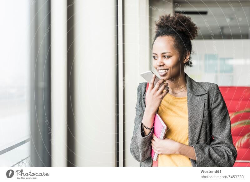 Junge Frau steht mit Smartphone am Fenster Zuversicht Zuversichtlich Selbstvertrauen selbstbewusst Vertrauen weiblich Frauen jung Handy Mobiltelefon Handies