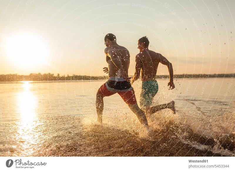 Zwei Freunde laufen im Wasser rennen Spaß Spass Späße spassig Spässe spaßig See Seen Freundschaft Kameradschaft Gewässer genießen geniessen Genuss