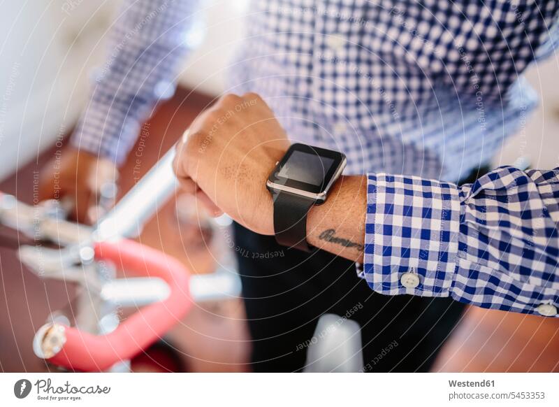 Nahaufnahme eines Mannes, der die Smartwatch kontrolliert, während er ein Fahrrad in der Wohnung hält Geschäftsmann Businessmann Businessmänner Geschäftsmänner