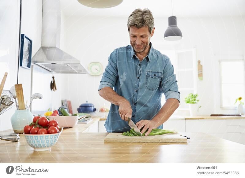 Reifer Mann in der Küche beim Gemüseschneiden Gemuese Tomate Speisetomaten Tomaten abschneiden kleinschneiden lächeln Männer männlich zubereiten kochen