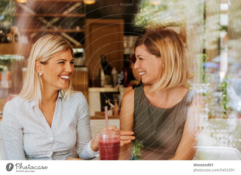 Zwei glückliche junge Frauen in einem Cafe lachen Freundinnen Spaß Spass Späße spassig Spässe spaßig sprechen reden Kaffeehaus Bistro Cafes Café Cafés