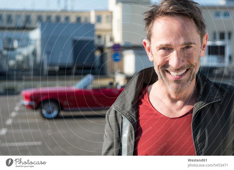 Porträt eines lächelnden reifen Mannes vor seinem Sportwagen auf der Parkebene Männer männlich Erwachsener erwachsen Mensch Menschen Leute People Personen