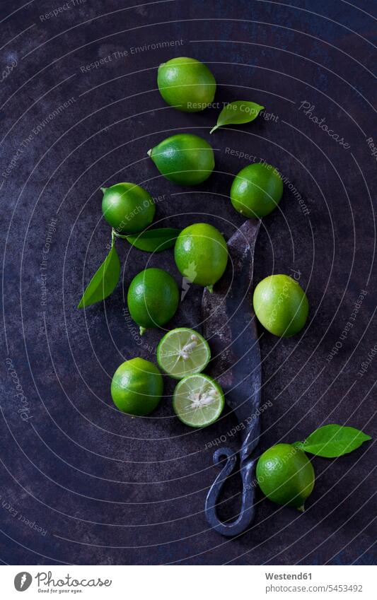 Geschnittene und ganze Limequats, Blätter und altes Messer auf dunklem Grund Niemand Zitrusfrucht Zitrusfruechte Zitrusfrüchte grün