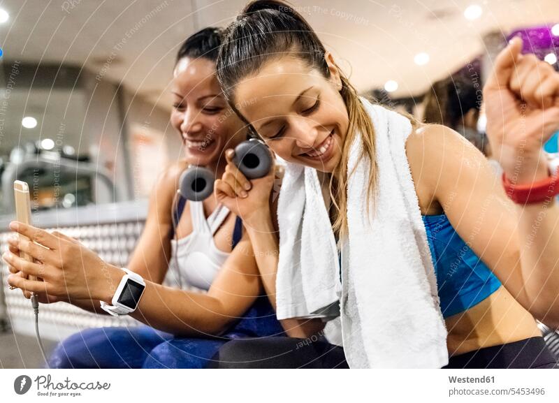 Zwei Frauen, die nach dem Training im Fitnessstudio Spaß mit ihrem Smartphone haben Pause glücklich Glück glücklich sein glücklichsein trainieren Handy