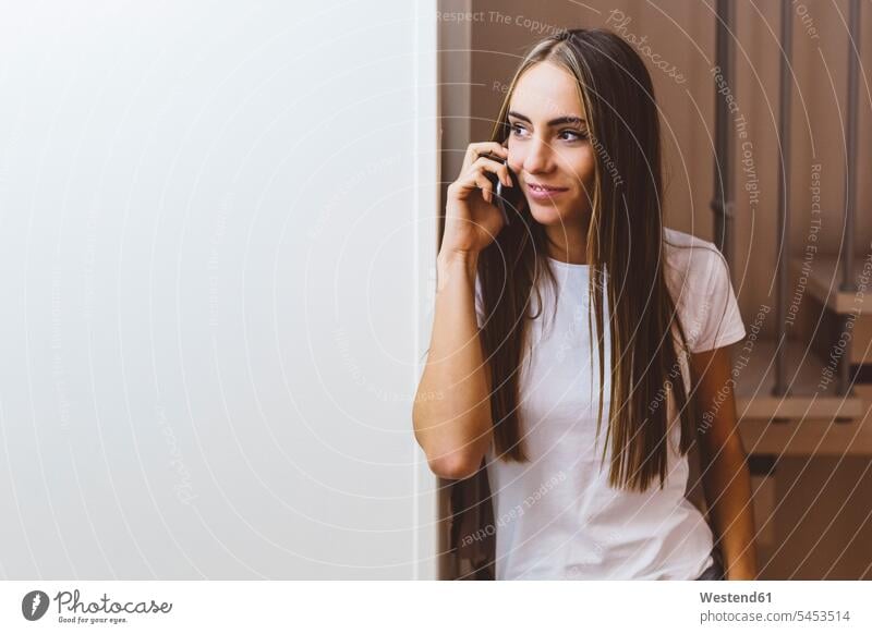 Lächelnde junge Frau zu Hause am Handy telefonieren anrufen Anruf telephonieren lächeln Zuhause daheim weiblich Frauen Telefon benutzen Erwachsener erwachsen