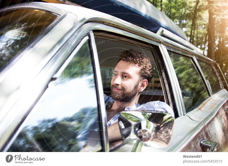 Lächelnder junger Mann im Auto im Wald Forst Wälder Wagen PKWs Automobil Autos lächeln Männer männlich Kraftfahrzeug Verkehrsmittel KFZ Erwachsener erwachsen