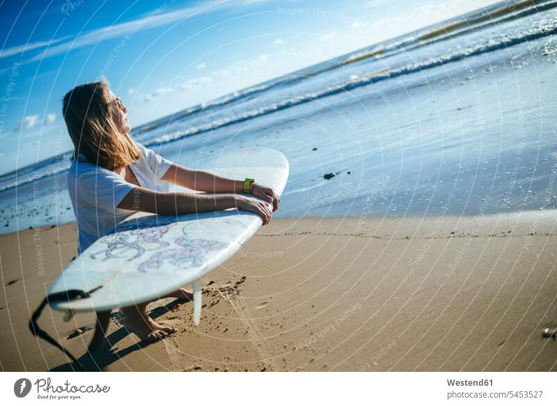 Junge Frau mit Surfbrett kauert am Strand und betrachtet den Sonnenuntergang Surferin Wellenreiterinnen Surferinnen Surfbretter surfboard surfboards Surfen