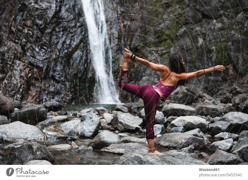 Italien, Lecco, Frau macht Lord of the Dance Yoga Pose auf einem Felsen in der Nähe eines Wasserfalls Yoga-Übungen Yogauebungen Yogaübungen Jogauebung