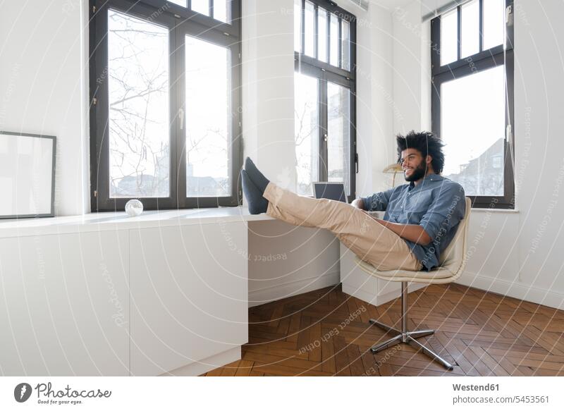 Mann sitzt in minimalistischem leeren Raum auf Stuhl Laptop Notebook Laptops Notebooks Männer männlich sitzen sitzend entspannt entspanntheit relaxt lächeln