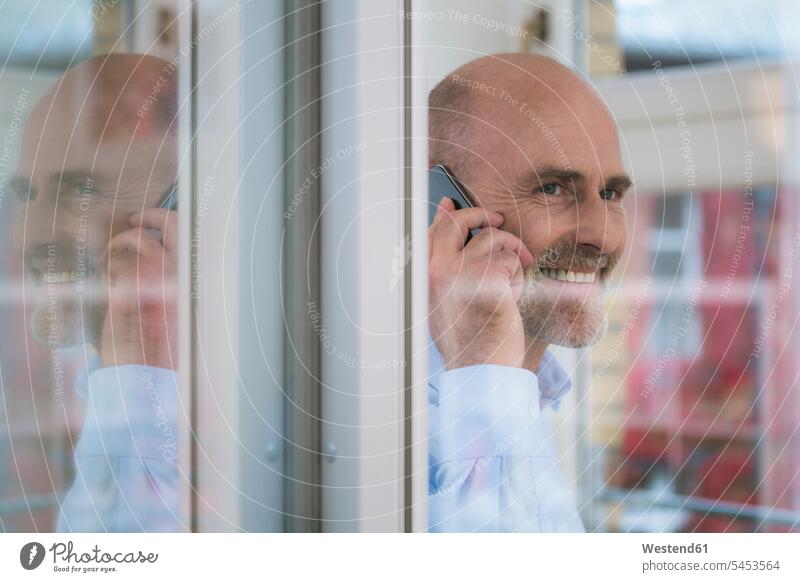 Lächelnder Geschäftsmann am Handy am Fenster lächeln Mobiltelefon Handies Handys Mobiltelefone telefonieren anrufen Anruf telephonieren Businessmann