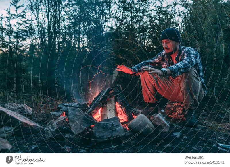 Mann sitzt am Lagerfeuer in ländlicher Landschaft sitzen sitzend Männer männlich Feuer Erwachsener erwachsen Mensch Menschen Leute People Personen Natur aktiv
