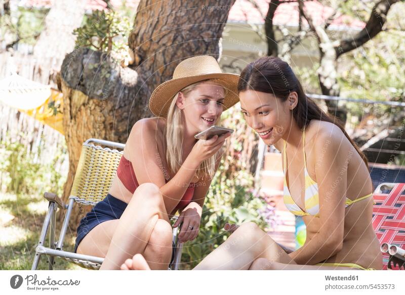 Zwei junge Frauen im Garten teilen sich ein Handy Freundinnen Mobiltelefon Handies Handys Mobiltelefone entspannt entspanntheit relaxt Freunde Freundschaft