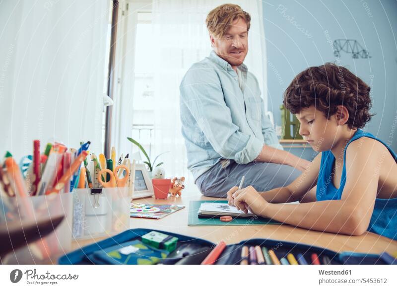 Vater hilft dem Jungen, seine Schularbeiten zu Hause zu erledigen erklären Hausaufgaben Sohn Eltern Familie Mensch Kind Unterstützung Innenaufnahme
