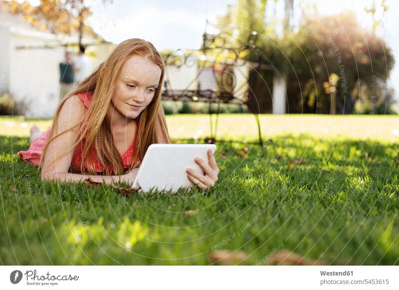 Grl mit langen roten Haaren im Gras liegend mit Tablette liegt Tablet Computer Tablet-PC Tablet PC iPad Tablet-Computer Mädchen weiblich entspannt entspanntheit