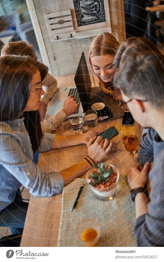 Gruppe von Freunden sitzt zusammen in einem Café mit Laptop, Smartphone und Getränken Cafe Kaffeehaus Bistro Cafes Cafés Kaffeehäuser sitzen sitzend Getraenk