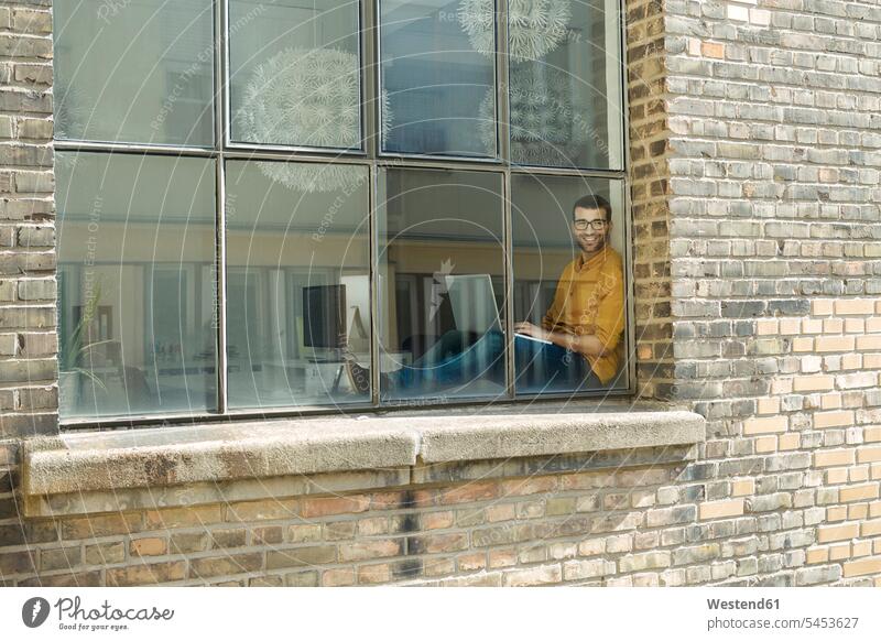 Junger Profi am Fenster, der selbstbewusst am Laptop sitzt Fensterbank Fensterbrett Fenstersims Fensterbänke Geschäftsmann Businessmann Businessmänner