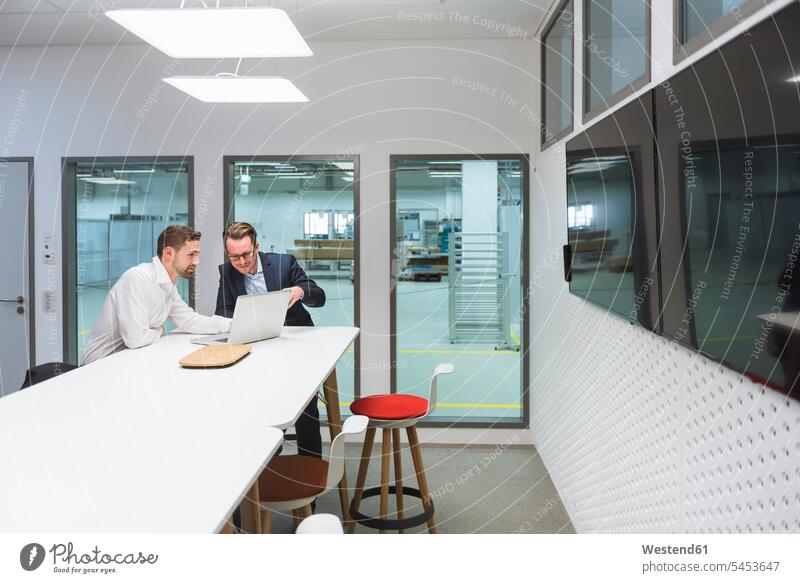 Zwei Geschäftsleute sitzen in einem modernen Büro und diskutieren vor einem Laptop Kollegen Arbeitskollegen Geschäftsmann Businessmann Businessmänner