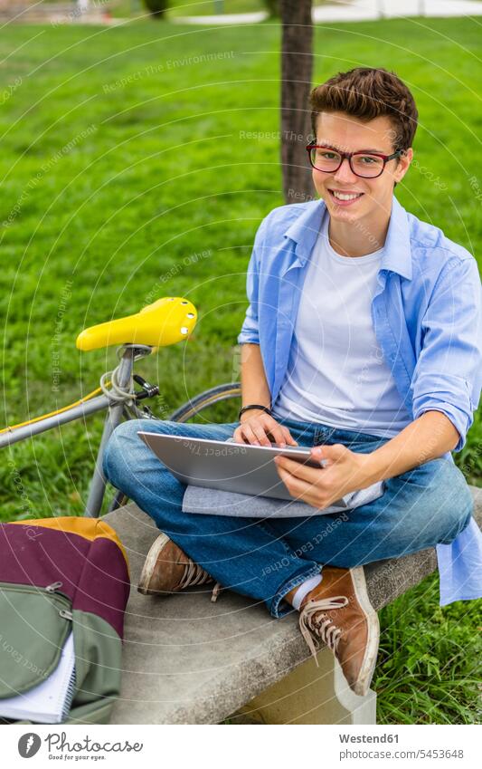 Porträt eines lächelnden jungen Mannes, der mit einem Laptop auf einer Bank sitzt Männer männlich Notebook Laptops Notebooks Erwachsener erwachsen Mensch