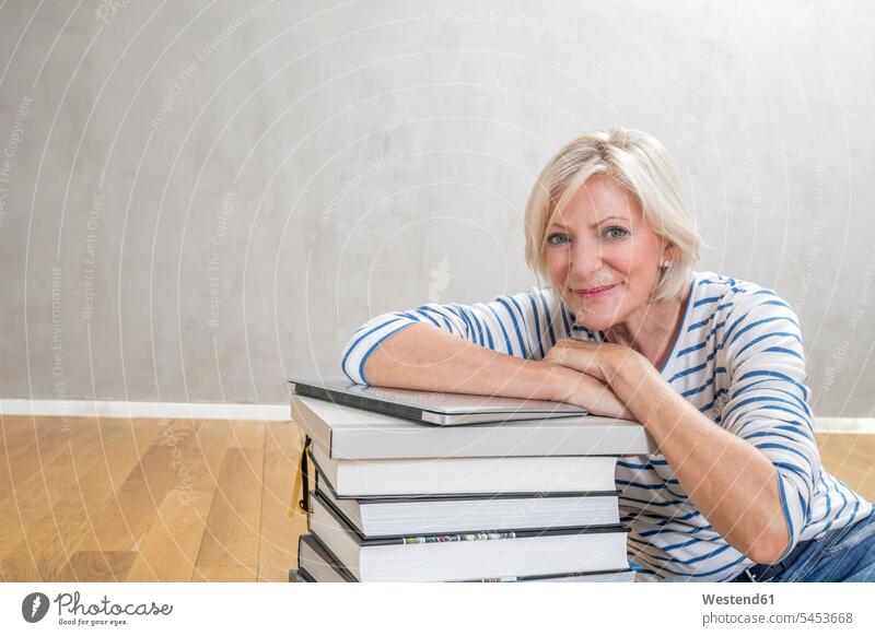 Porträt einer lächelnden älteren Frau, die sich an einen Stapel Bücher und einen Laptop lehnt Portrait Porträts Portraits gestapelt Haufen Notebook Laptops