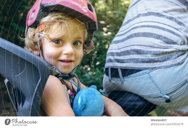 Bildnis eines kleinen Mädchens mit Helm, das mit seinem Vater auf einem Kindersitz für Fahrrad sitzt Helme Bikes Fahrräder Räder Rad lächeln weiblich Papas