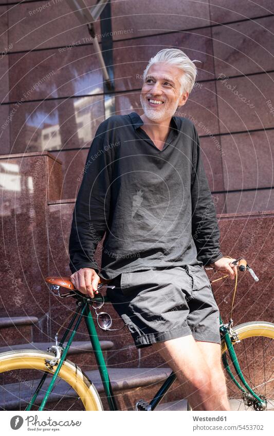 Reifer Mann in der Stadt, der sich auf sein Fahrrad stützt Bikes Fahrräder Räder Rad Männer männlich radfahren fahrradfahren radeln unterwegs auf Achse