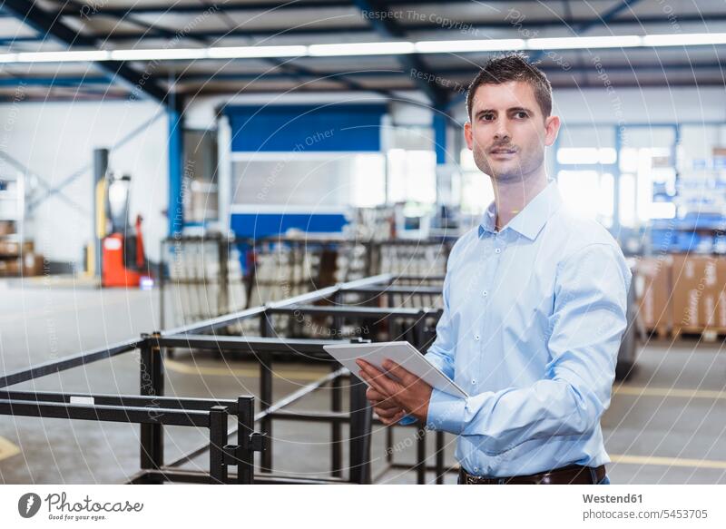 Junger Mann arbeitet in der Werkstatt und benutzt ein digitales Tablett stehen stehend steht Angestellter Mitarbeiter Fabrik Fabrikgebäude Fabrikgebaeude