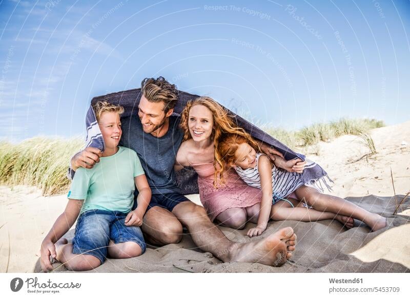 Niederlande, Zandvoort, glückliche Familie unter einer Decke am Strand lächeln Beach Straende Strände Beaches Familien Glück glücklich sein glücklichsein Mensch