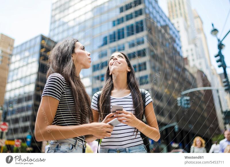 USA, New York City, zwei Zwillingsschwestern mit Mobiltelefonen in Manhattan schauen auf Freundinnen Handy Handies Handys Schwester Schwestern Spaß Spass Späße