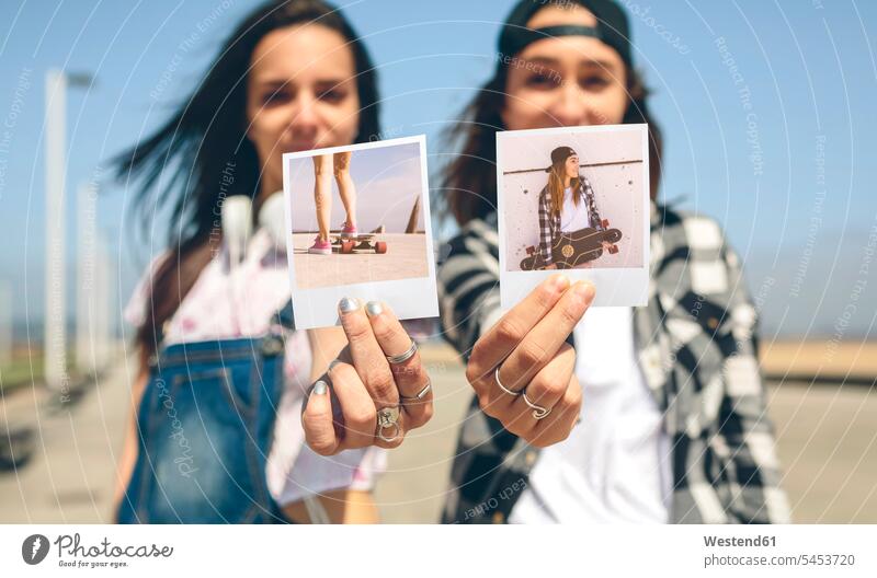 Zwei junge Frauen zeigen Sofortfotos mit ihren Longboards Europäer Kaukasier Europäisch kaukasisch beste Freundin beste Freundinnen weiblich Gemeinschaft