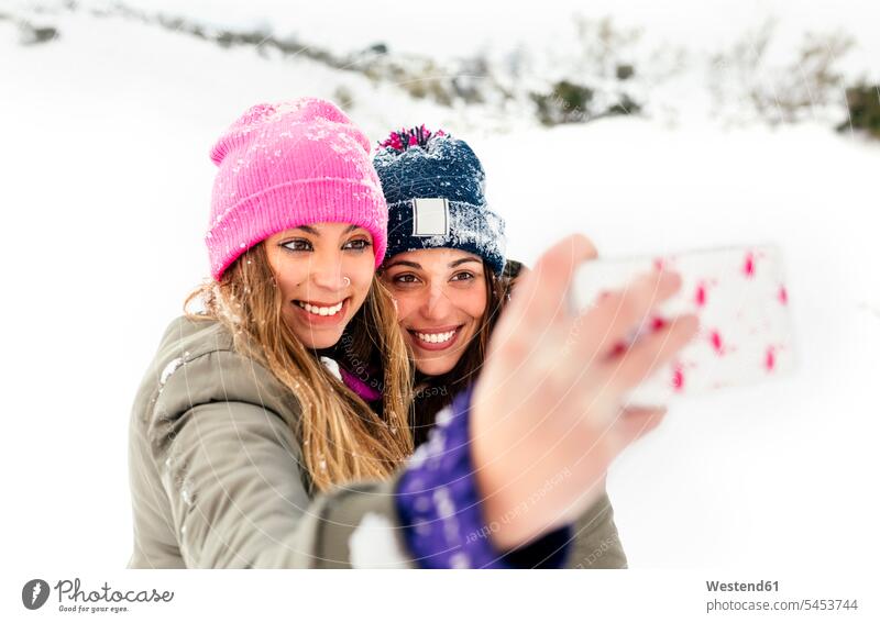 Zwei Freunde machen Selfies mit dem Smartphone im Schnee Winter winterlich Winterzeit Freundschaft Kameradschaft Handy Mobiltelefon Handies Handys Mobiltelefone