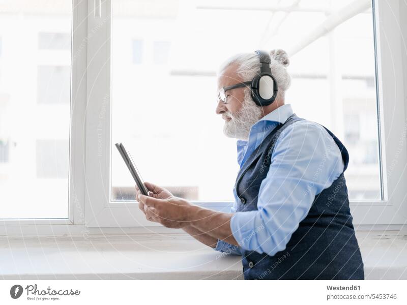 Reifer Mann mit Tablette und Kopfhörer am Fenster hören hoeren Kopfhoerer Männer männlich Tablet Computer Tablet-PC Tablet PC iPad Tablet-Computer Erwachsener