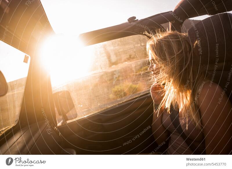 Blonde Frau mit wehendem Haar sitzt im Auto und genießt den Sonnenuntergang wehende Haare wehendes Haar blond blonde Haare blondes Haar weiblich Frauen sitzen