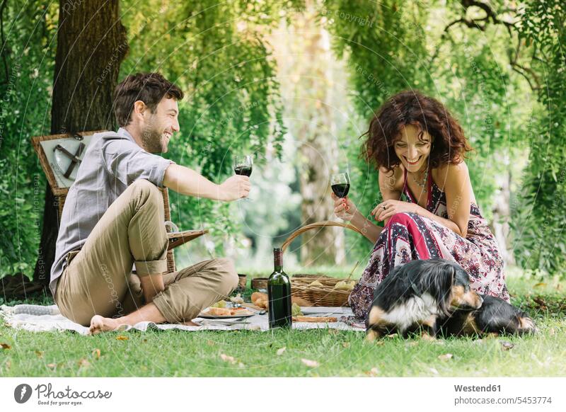 Pärchen mit Hund beim Picknick in einem Park bei Rotwein Hunde picknicken Parkanlagen Parks lächeln Paar Paare Partnerschaft Wein Weine Haustier Haustiere Tier