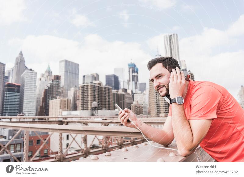 USA, New York City, Sportler auf der Brooklyn Brige mit Handy und Kopfhörern Kopfhoerer Brücke Bruecken Brücken Mann Männer männlich Joggen Jogging hören hoeren
