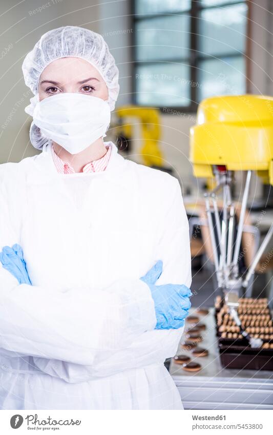 Porträt einer Frau in Arbeitsschutzkleidung mit einem Roboter, der mit Keksen hantiert, im Hintergrund weiblich Frauen Plaetzchen Plätzchen Fabrik Fabriken