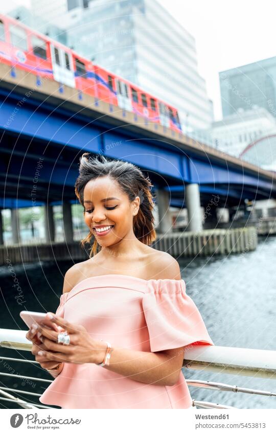 Lächelnde Frau, die in der Stadt mit ihrem Smartphone Nachrichten verschickt lächeln Handy Mobiltelefon Handies Handys Mobiltelefone weiblich Frauen Telefon